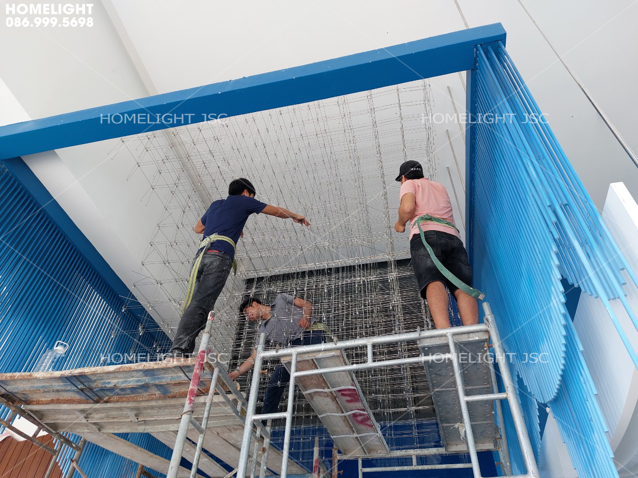 Hai thợ HomeLight đứng trên giàn giáo treo từng sợi đèn thả, thi công đèn chùm sảnh khách sạn Scenia Bay