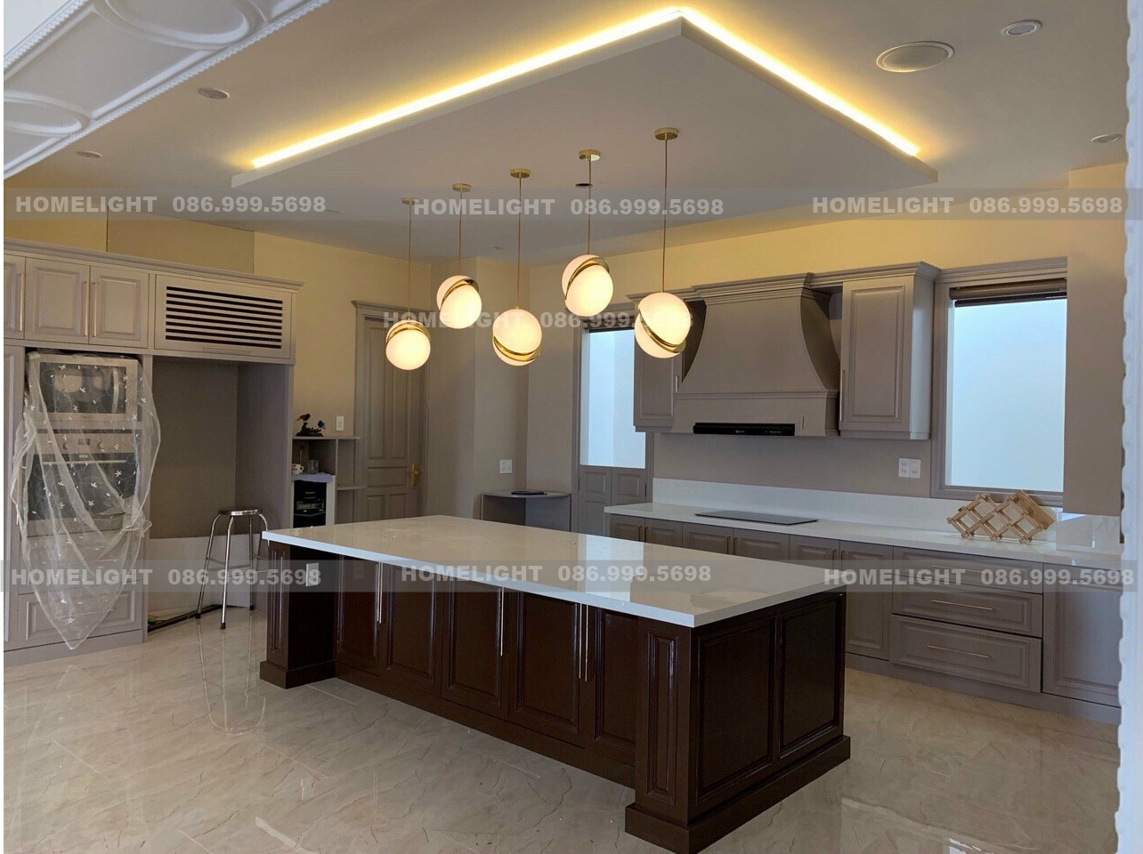 Năm đèn thả cầu thủy tinh trắng viền vàng treo so le trên đảo bếp mặt đá trắng, cách xếp nhiều bóng giống đèn thả bàn ăn cho bàn dài