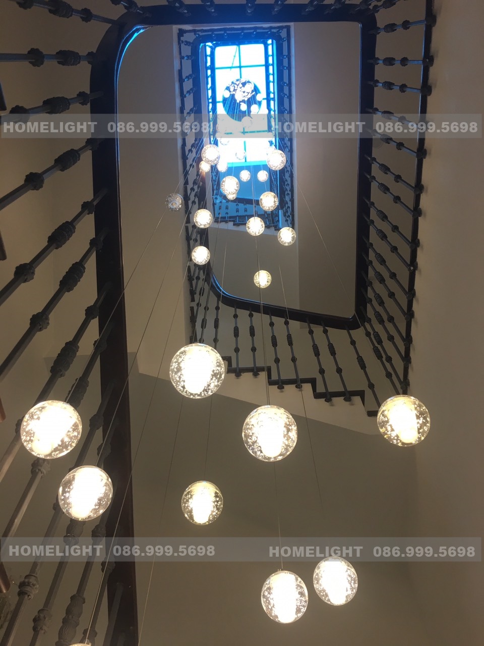 Đèn treo trần dạng quả cầu thủy tinh bọt khí thả dọc giếng cầu thang, nhìn từ dưới lên tới cửa sổ trên cùng, công trình HomeLight lắp ở biệt thự Starlake