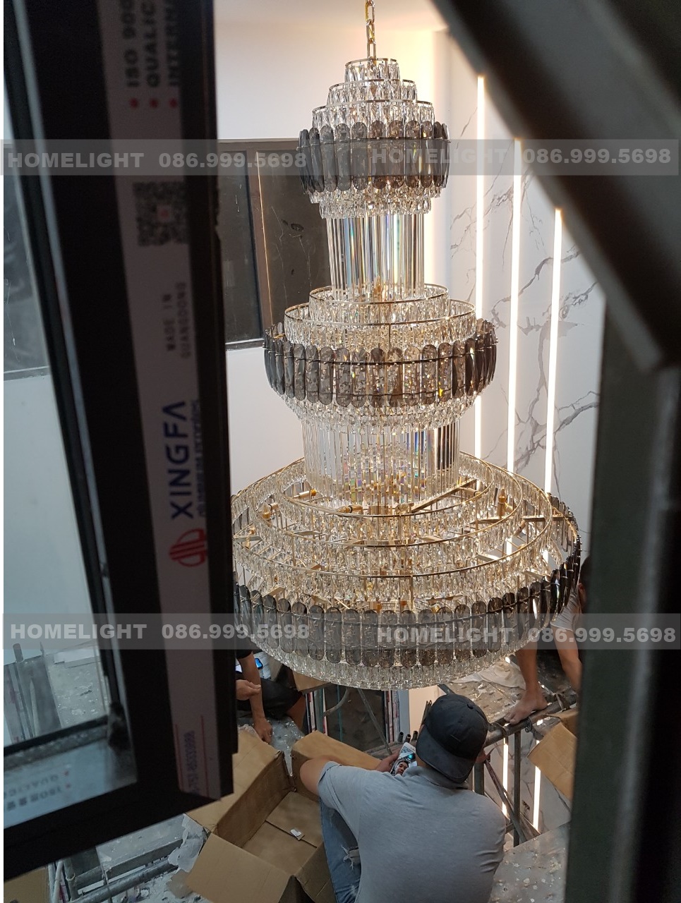Đèn chùm thông tầng pha lê nhiều tầng đang lắp pha lê, chụp qua cửa sổ tầng trên của Villa Thạch Thất