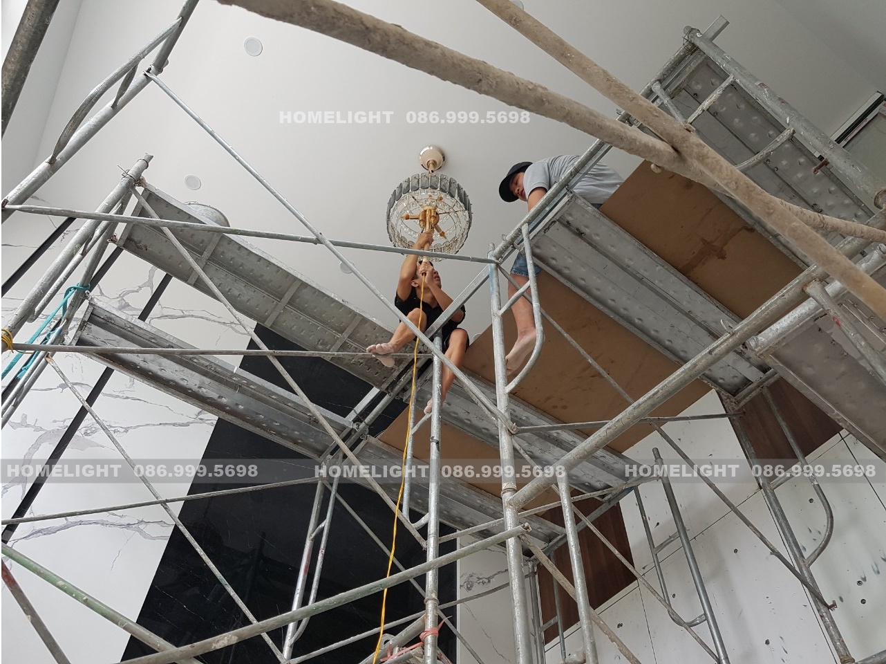 Thợ HomeLight trên giàn giáo treo tầng trên cùng của đèn chùm thông tầng lên trần, dây điện thả dọc xuống, công trình Villa Thạch Thất